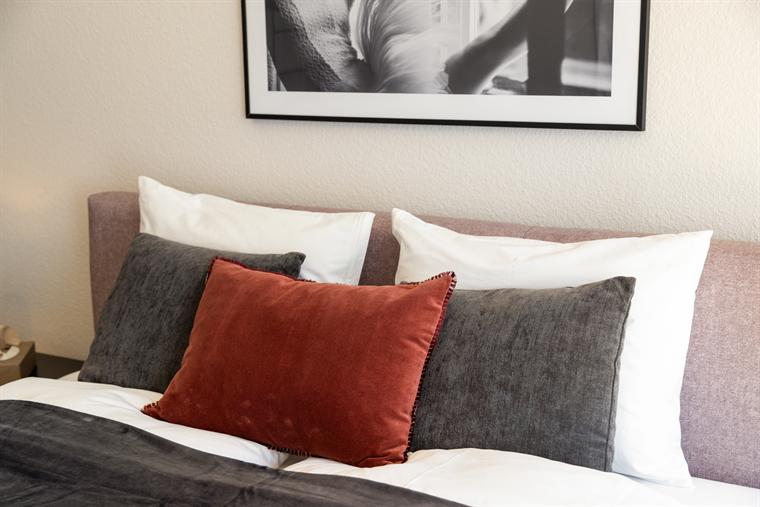 Bett mit rostrotem Kissen vor einer Schwarz-Weiss-Fotografie